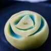 Handmade green nerikiri wagashi shaped like a blooming flower on a dark plate